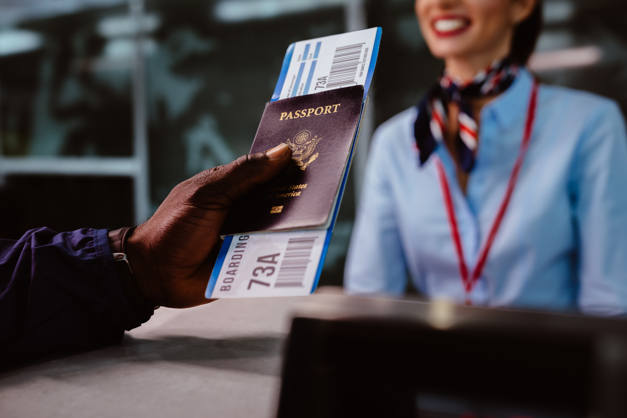 nærbillede af en mandlig hånd, der holder et pas og en flybillet og rækker ud mod en stewardesse ved en skranke