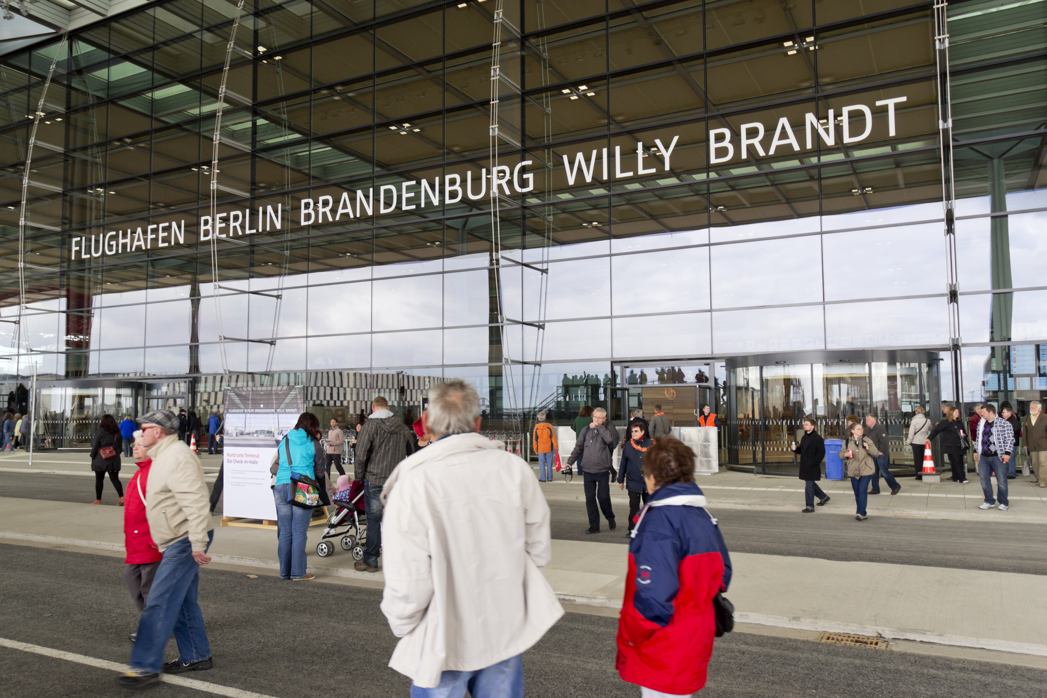 Der Haupteingang des Flughafens Berlin Brandenburg Willy Brandt mit vielen Leuten im Vordergrund.