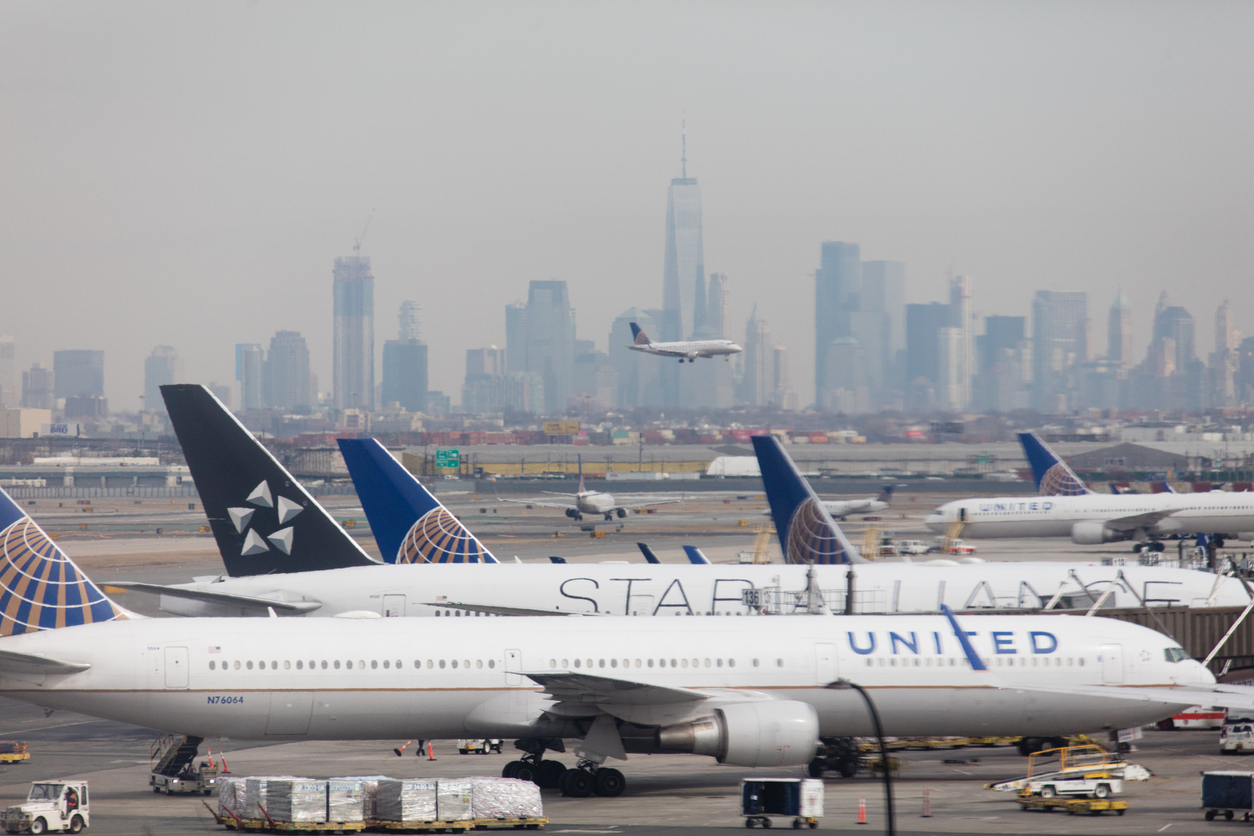 Ein Rollfeld mit einem landenden Flugzeug und der Skyline von Manhattan im Hintergrund.