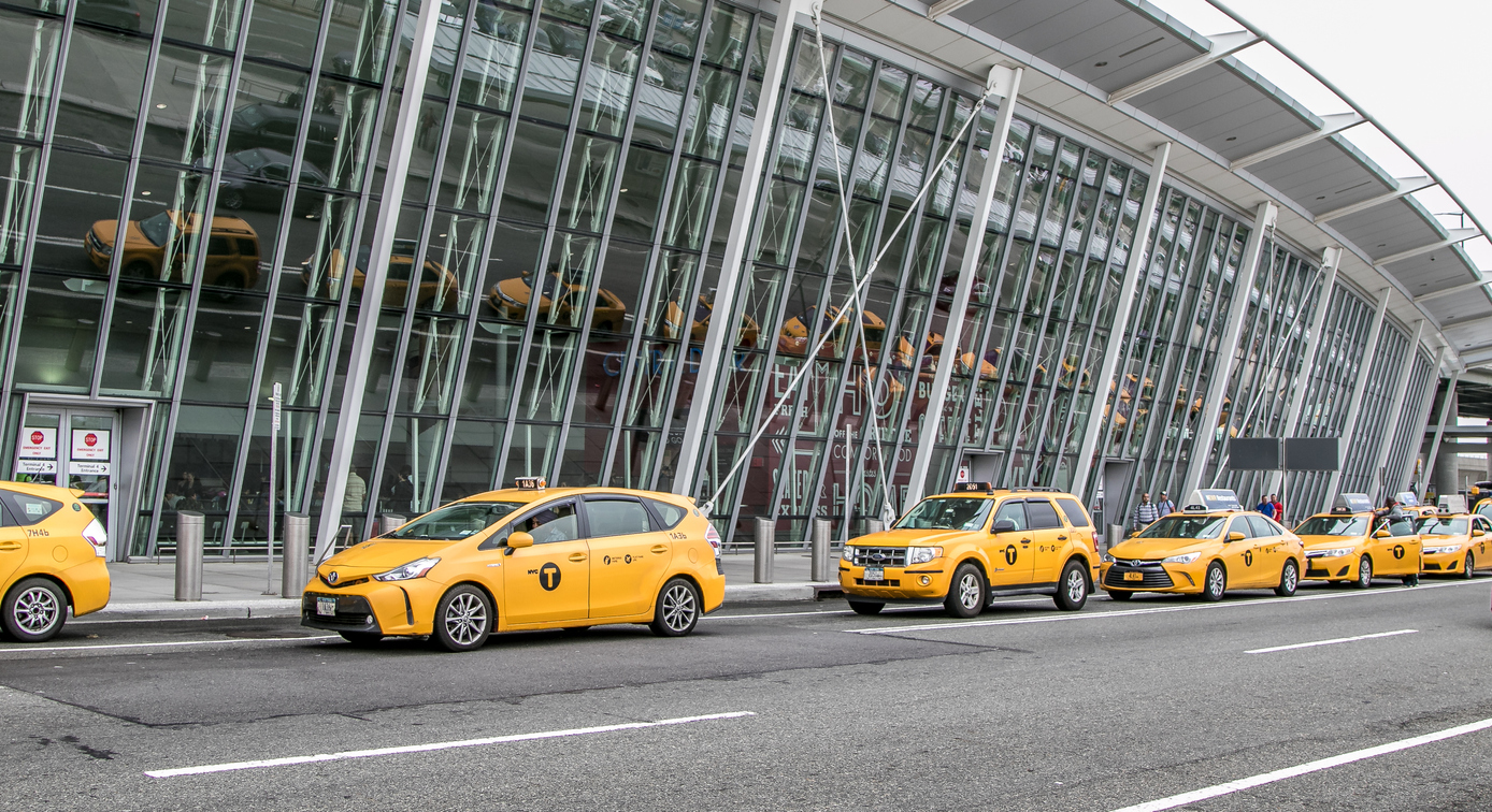 Mehrere parkende Yellow Cabs aufgereiht vor einem New Yorker Flughafen.