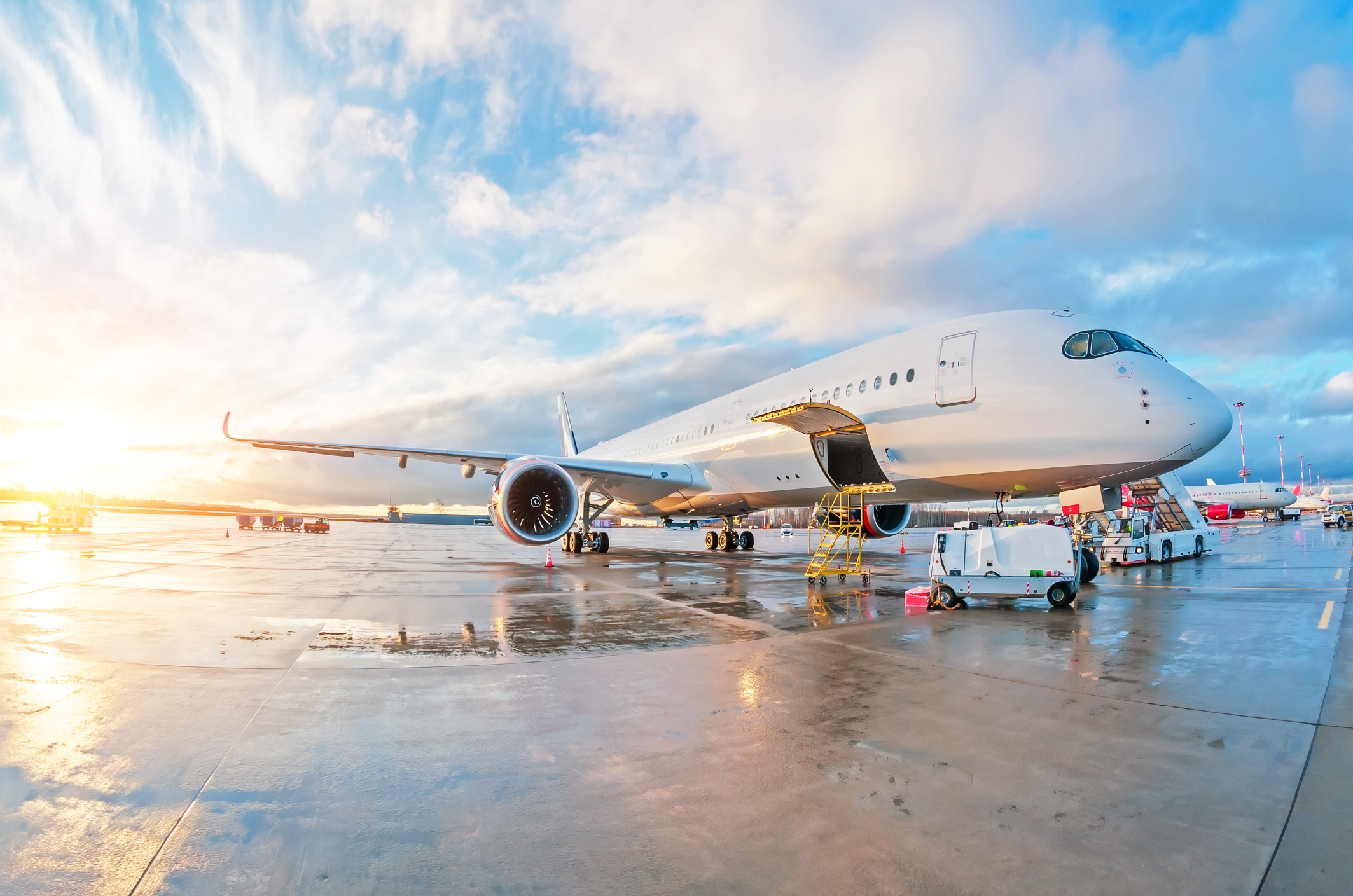 Wartungsarbeiten an einem geparkten Passagierflugzeug auf nassem Grund am Flughafen bei Sonnenuntergang