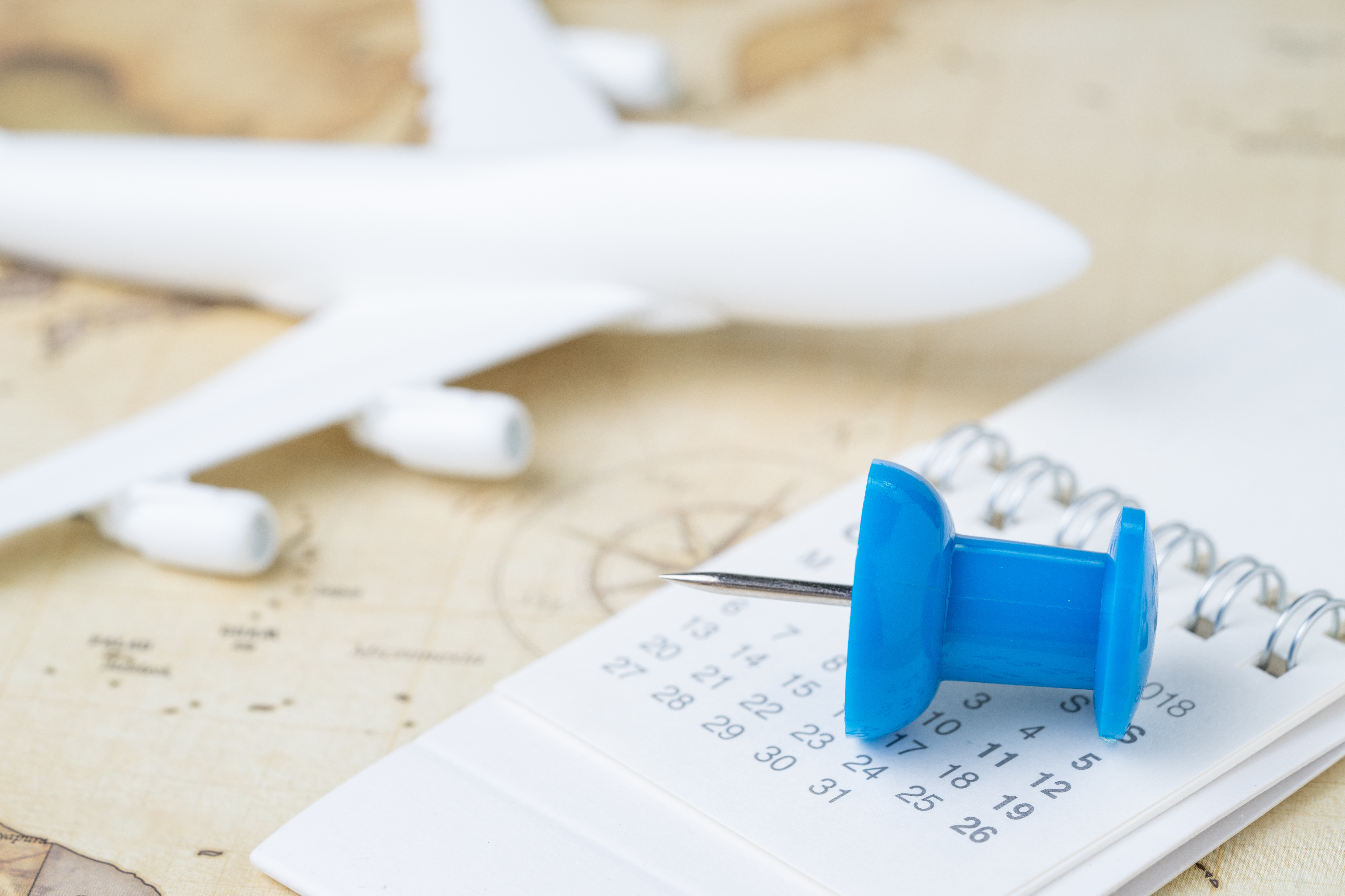 Åben kalender med en blå nål i fokus med en sløret flyvemaskine på et kort i baggrunden