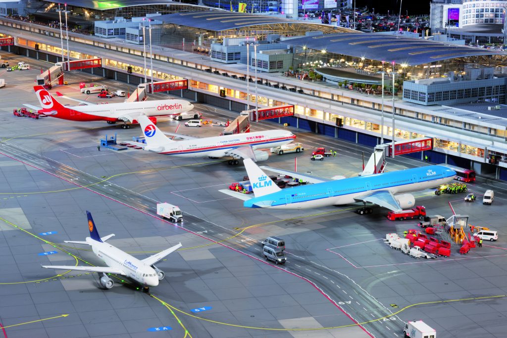 Mehrere Flugzeuge stehen mit angedockten Gangways an den Gates, im Vordergrund fährt eine Lufthansa-Maschine, im Hintergrund befinden sich die Terminals.