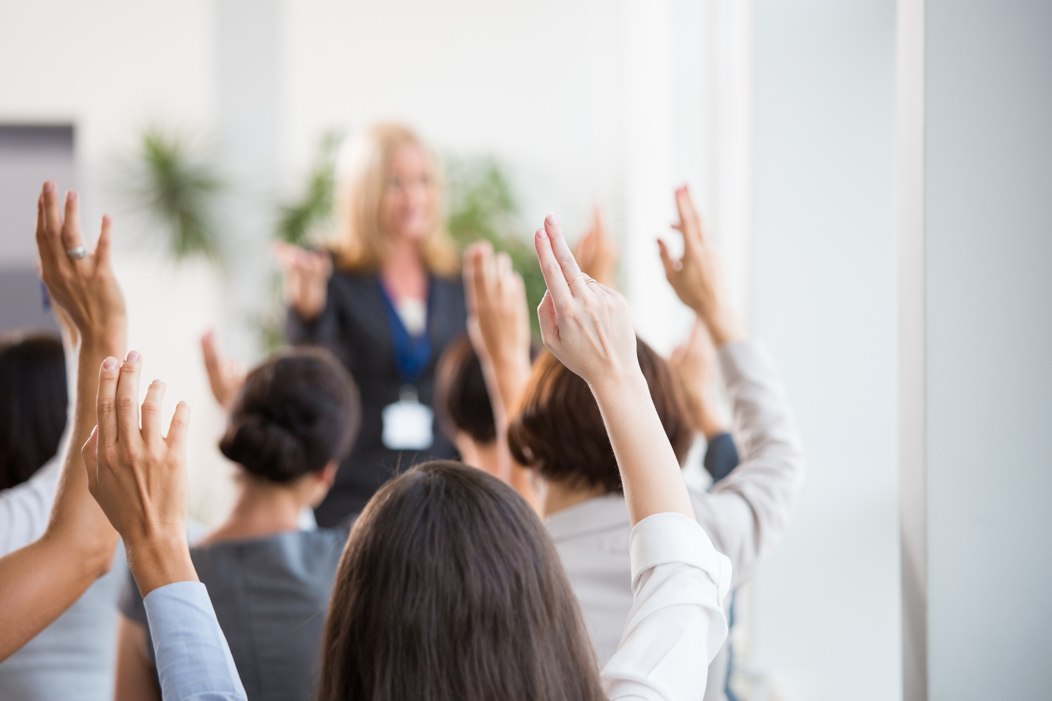 mehrere Menschen, die mit gehobener Hand auf einer Kofferauktion für ein bestimmtes Produkt bieten und mit dem Körper der Auktionatorin zugewandt sind