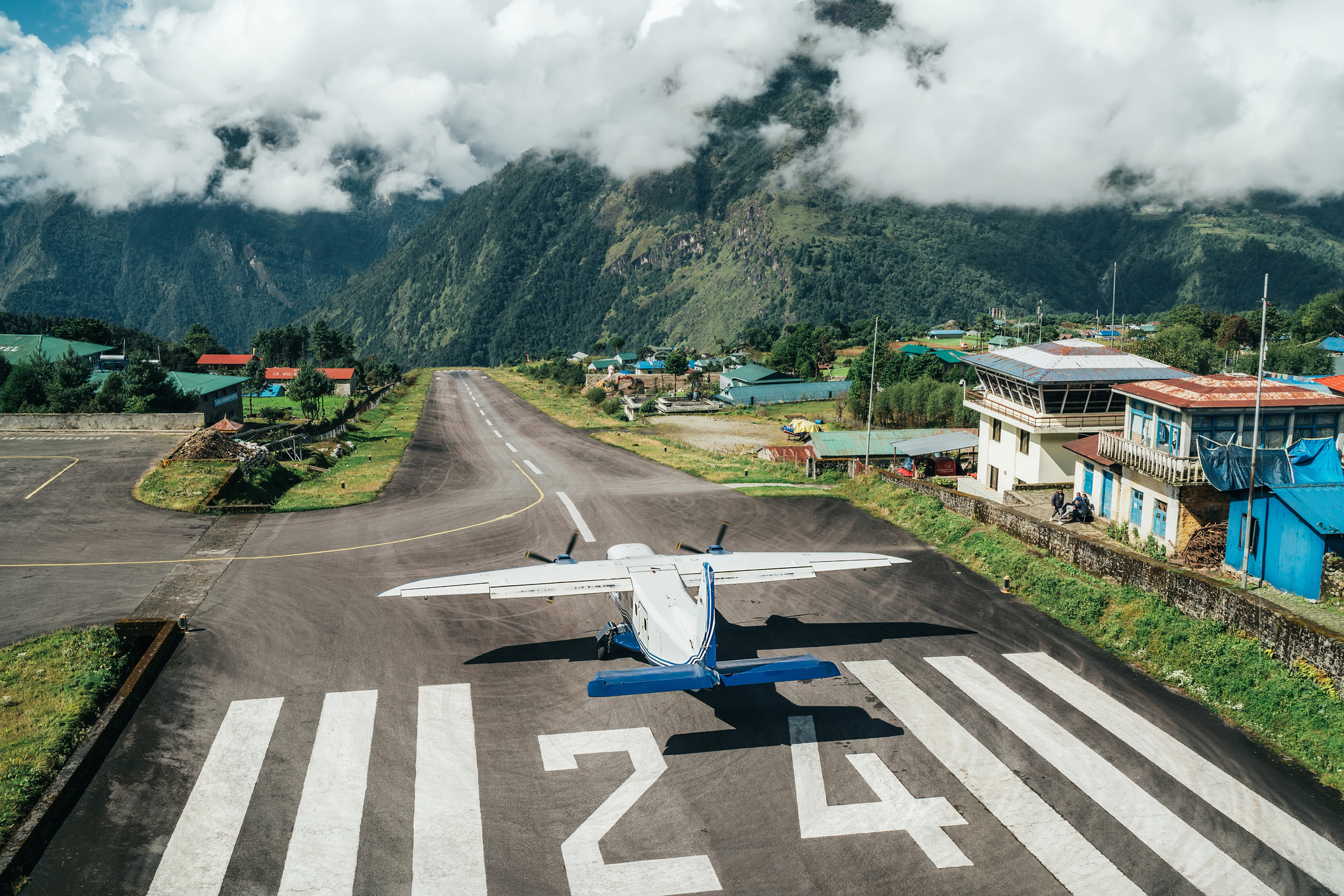 Die Startbahn in Lukla mit Sonne aber auch einigen tiefhängenden Wolken, ein Propellerflugzeug beginnt gerade den Start.