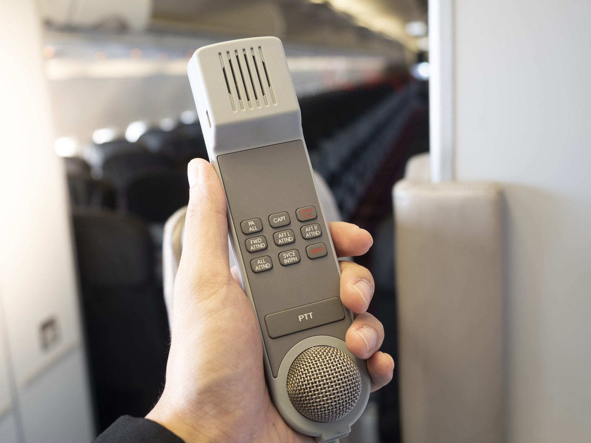 Männlicher Flugbegleiter hält in seiner Hand eine Sprechanlage in der Flugzeugkabine