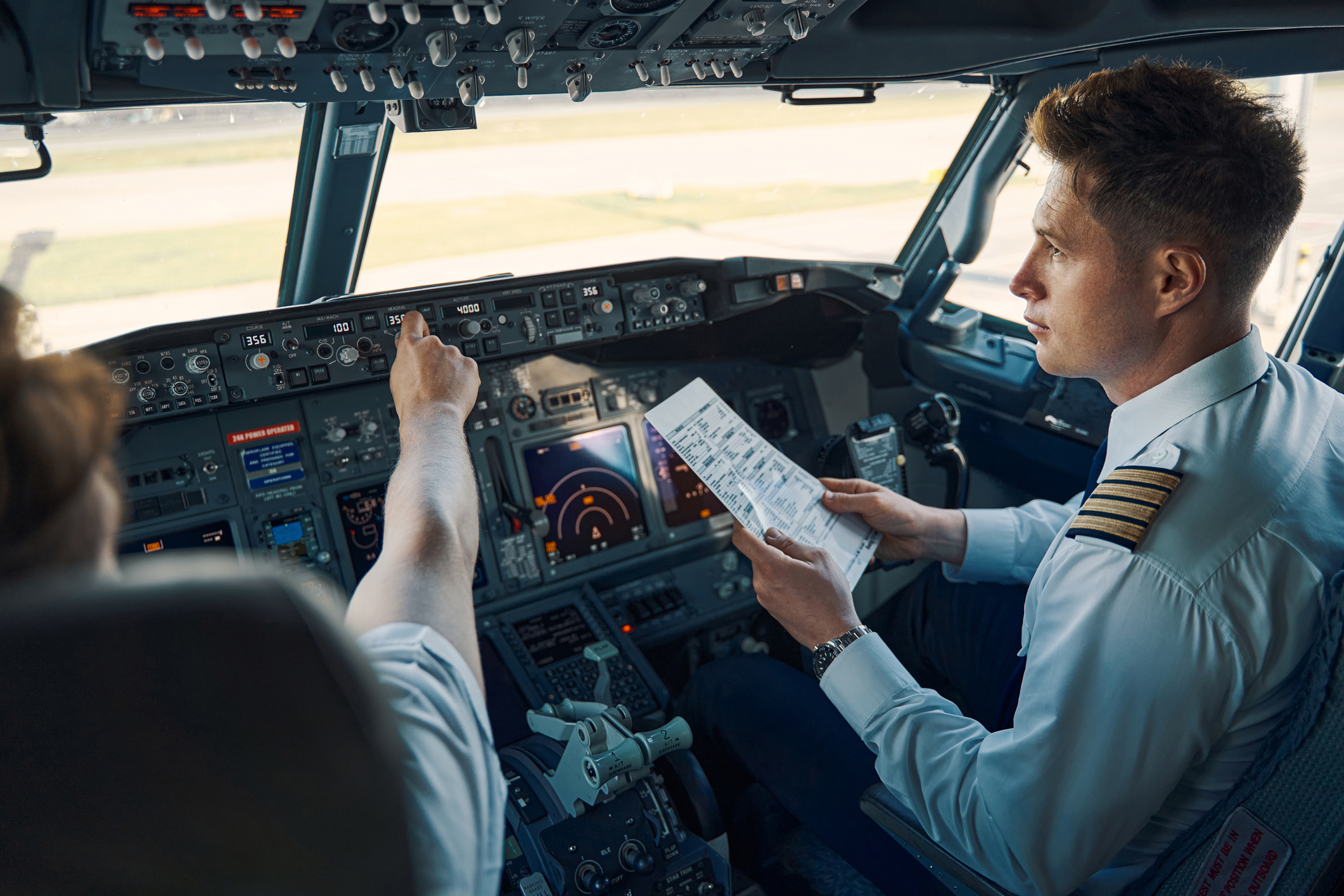 Co-Pilot mit einer Checkliste für den Flug in der Hand, der neben dem Chefpiloten im Cockpit sitzt