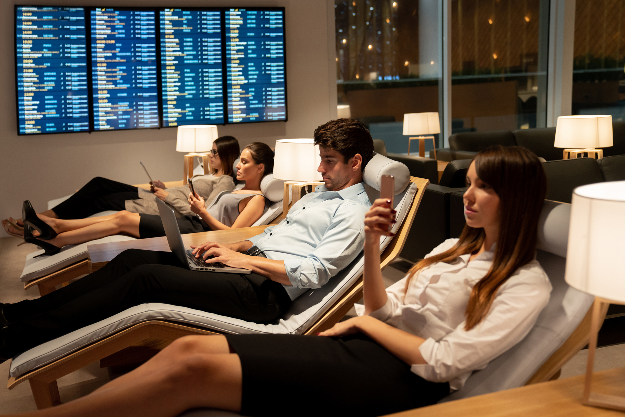 schick gekleidete Geschäftsreisende, die sich in einer VIP-Lounge am Flughafen entspannen und an ihrem Handy oder Laptop sind, während sie auf ihren Flug warten
