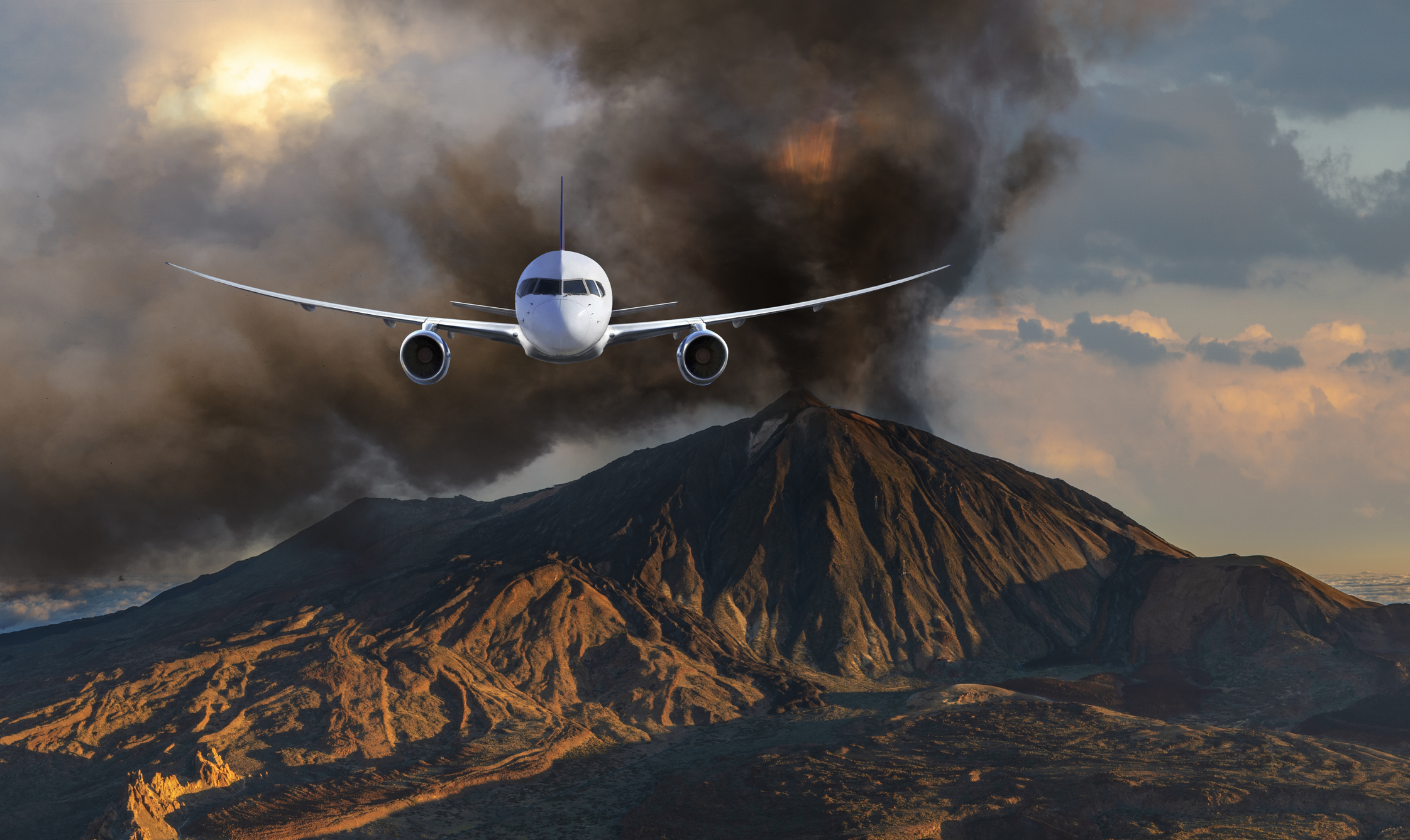 Ein Flugzeug fliegt auf die Kamera zu, im Hintergrund sind eine Aschewolke und Vulkanlandschaft zu sehen.