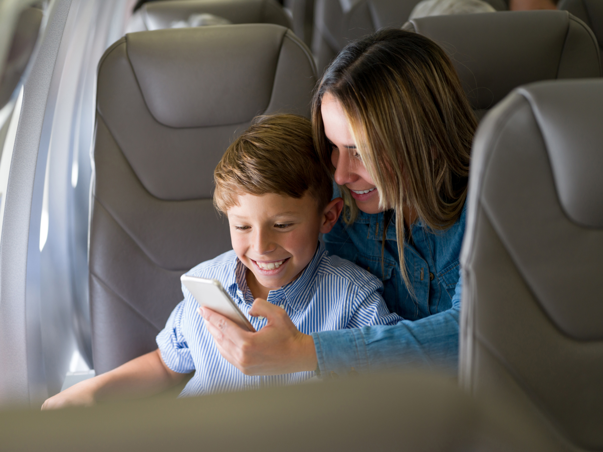 Moeder en zoon samen aan de mobiele telefoon in het vliegtuig