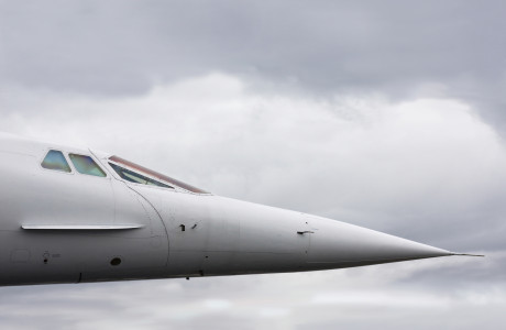 The nose and cockpit of a Concorde in front of a cloudy sky.
