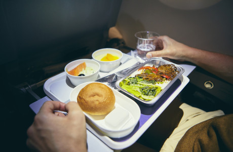 Nahaufnahme eines Tabletts, auf dem Abendessen in der Economy Class auf einem Langstreckenflug inklusive eines Getränks enthalten sind