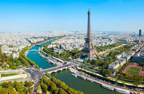 Eine Luftaufnahme von Paris, im Vordergrund sind der Eiffelturm und die Seine zu sehen, im Hintergrund erstreckt sich die Stadt.