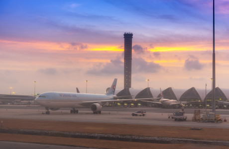 I skumringen står et Korean Air-fly på landingsbanen i forgrunden, mens lufthavnstårnet i Bangkok Suvarnabhumi Airport rejser sig i luften i baggrunden.