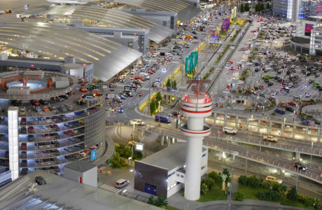 Die Front der Terminals des Knuffingen Airports mit Parkplätzen, Parkhaus und zahlreicher Autos auf den Straßen.