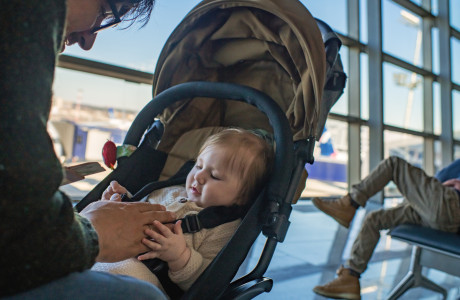 Ein Mann sitzt an einem Flughafen-Terminal und spielt mit einem Baby in einem Kinderwagen.